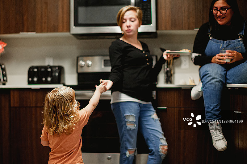 两个成年妇女和蹒跚学步的女孩在家庭厨房一起享受牛奶和饼干图片素材