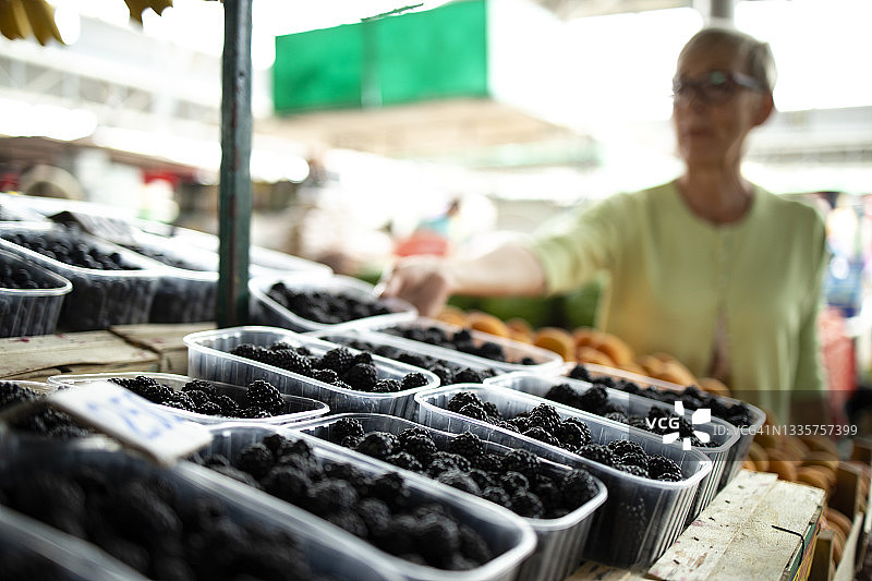 一个白人妇女在市场买新鲜的有机黑莓和水果，手里拿着满满一袋的健康食品。图片素材