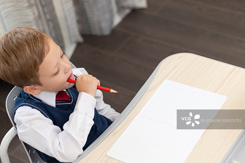 身穿校服的一年级男生在家里拿着铅笔坐在书桌前做作业。远程教育。有选择性的重点。特写镜头图片素材