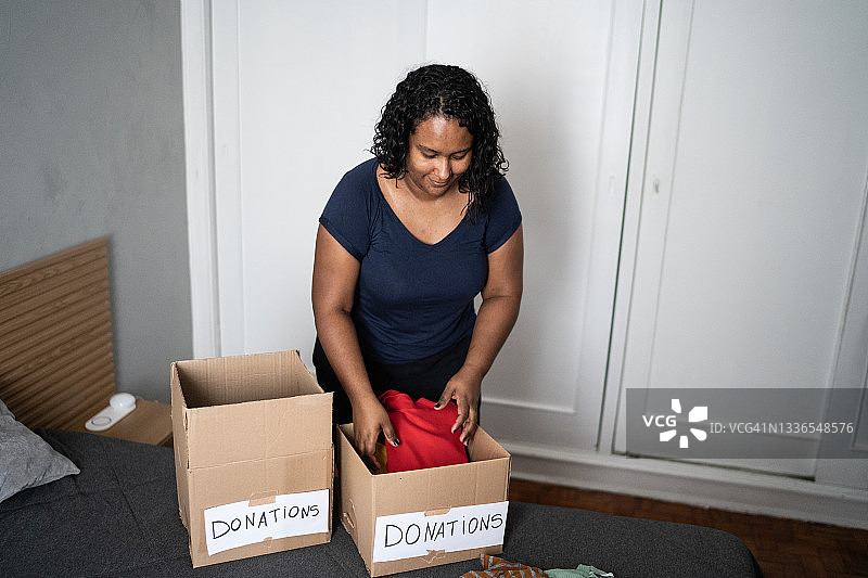 一名妇女正在整理箱子里的衣服，准备在家捐赠图片素材