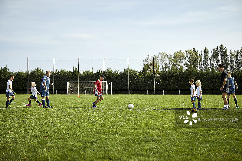 男教练在球场上教孩子们踢足球图片素材
