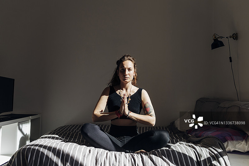 女人双手合十坐在床上练习瑜伽图片素材