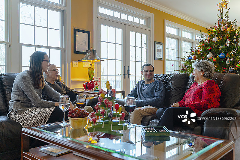 在圣诞节的时候家人团聚。两代人围坐在宽敞的客厅里的咖啡桌旁，旁边摆着一棵装饰精美的巨大圣诞树。图片素材