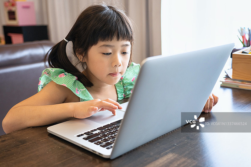 儿童在线教育。一个小女孩家里有一台笔记本电脑。快乐的小孩在室内玩电脑。图片素材