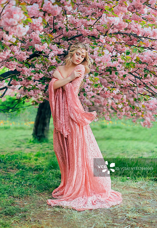 幻想幸福的女公主依偎在春暖花开的花园中。粉红色的花樱花树夏天自然。长蕾丝裙，宽袖子随风飘动。金发女孩女王。图片素材