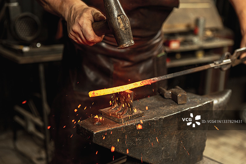 近距离工作的男性铁匠有力的手锻造一个铁匠的铁产品。铁锤，炽热的金属和铁砧。劳动概念，复古的职业图片素材