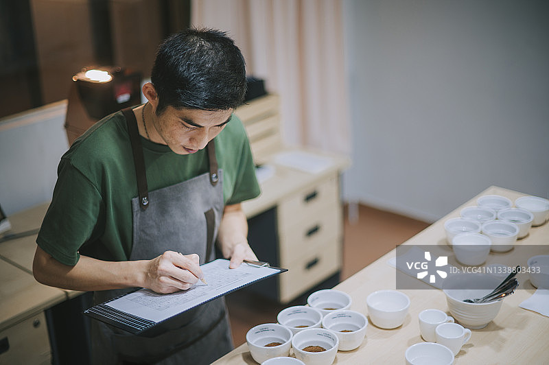 高角度专业亚洲华人咖啡师品级表演咖啡杯后写在剪贴板上图片素材
