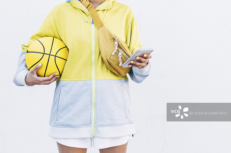 年轻女子拿着篮球在白墙前用智能手机图片素材