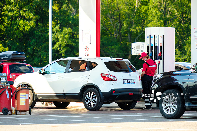 一名身穿制服的女性油罐车在加油站为一辆汽车加油。图片素材