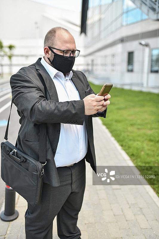 戴着口罩的秃顶商人使用智能手机在旅途中做生意图片素材