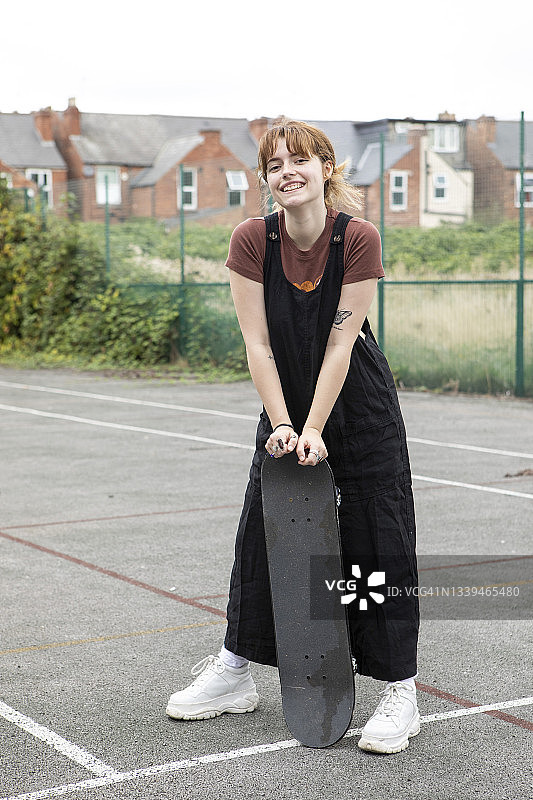 女学生站在一个废弃的网球场滑板在一个城市图片素材