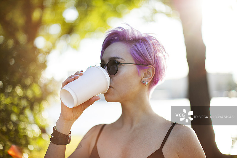 一个年轻的成年女子在公园里喝着咖啡图片素材