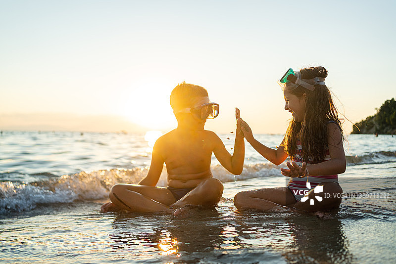 日落时分，兄妹俩坐在沙滩上玩小石子图片素材