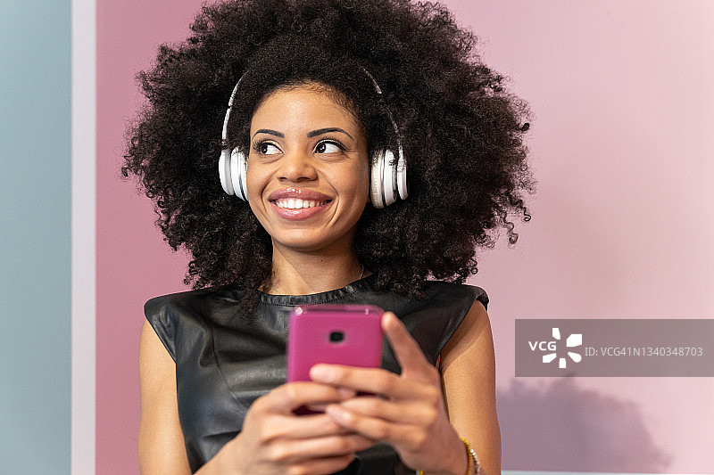 开朗的非洲裔美国年轻女子，留着非洲式的发型，戴着白色无线耳机，在录音室里拿着电话图片素材