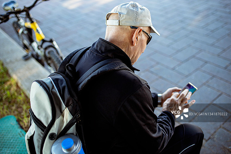 老男人骑自行车休息时，用手机上网图片素材