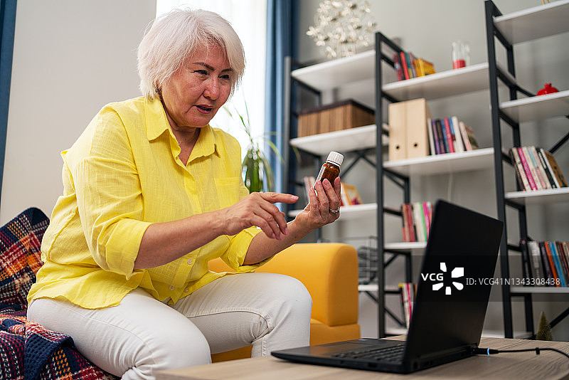 侧视老年妇女在笔记本电脑上进行视频通话，居家在线医疗数字技术服务咨询图片素材