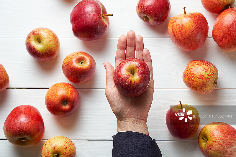 红色的苹果，白色木制背景。一个女人或女孩手里拿着水果，背景是厨房的餐桌。有机农场生态产品的种植。素食、纯素、生食、饮食的概念。图片素材
