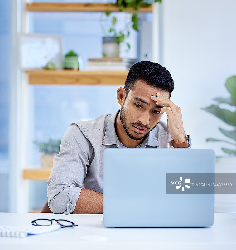一名年轻的商人在办公室里用笔记本电脑工作，看上去压力很大图片素材