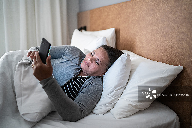 一个成熟的女人躺在床上玩手机图片素材