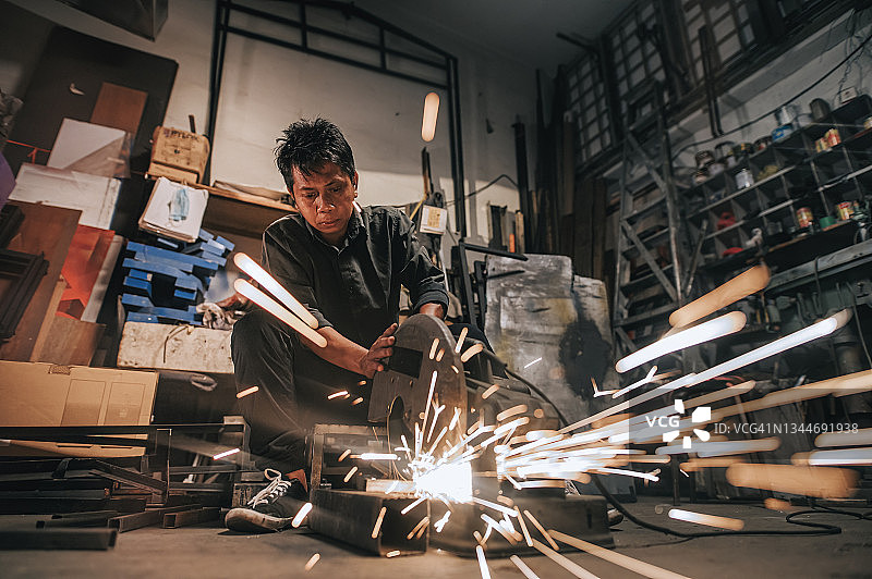 亚洲马来人成熟的焊工在车间用磨床焊接切割金属图片素材