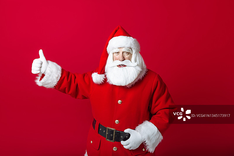 快乐的圣诞老人肖像兴高采烈地显示背书“喜欢”的标志在红色背景马圣诞快乐和新年图片素材