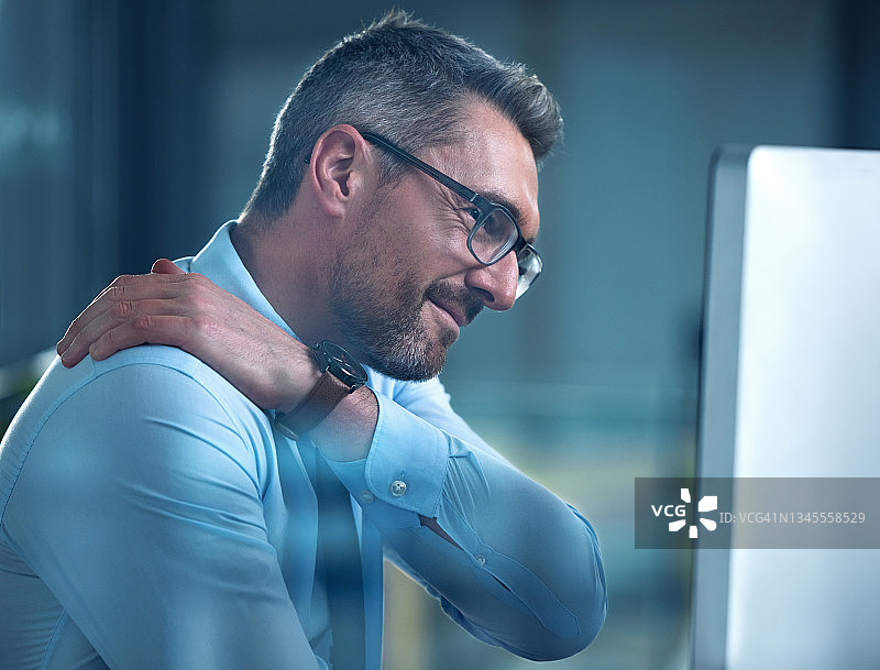 一张商人在办公桌前工作时肩膀疼痛的照片图片素材