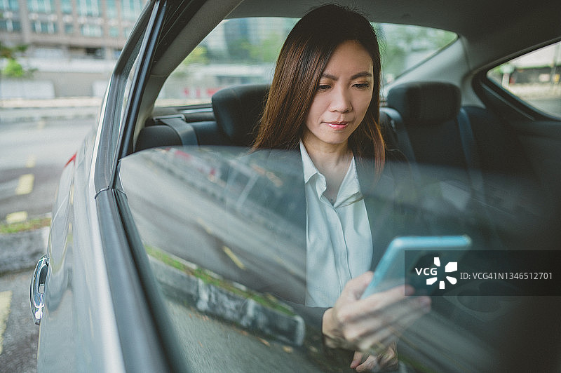美丽的亚洲女商人在汽车后座用智能手机发短信图片素材