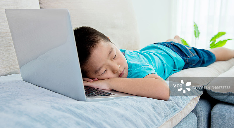 小男孩睡在笔记本电脑旁图片素材