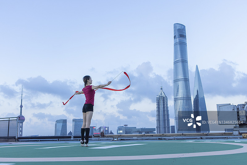 中国上海，一名年轻的女芭蕾舞者在屋顶上用红丝带跳舞图片素材