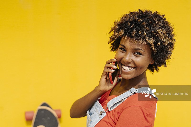 一位非洲裔美国妇女在户外大街上讲电话时面带微笑看着镜头。图片素材