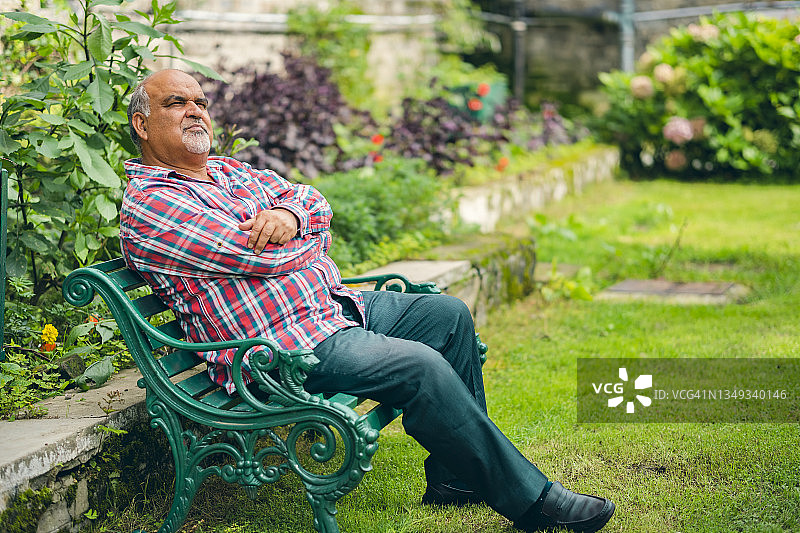 一位老人在草地上的长椅上休息。图片素材
