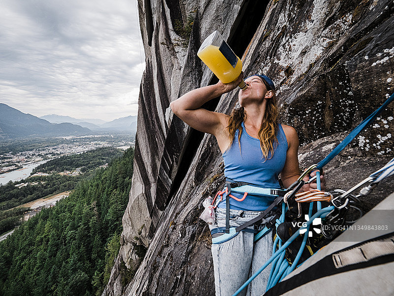 一位强壮的女攀岩者在高高的岩壁上喝着水壶里的果汁图片素材
