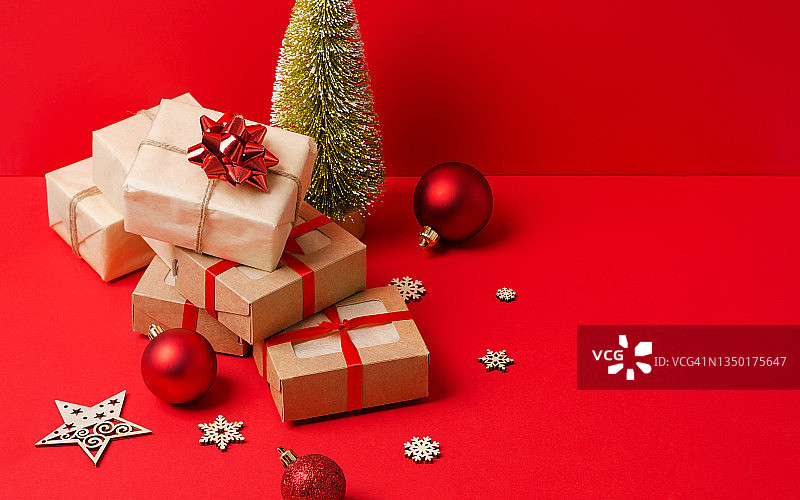 一堆装在牛皮纸和牛皮纸盒子里的礼物，红色背景上装饰着圣诞树的木质生态装饰。圣诞节背景，节礼日，圣诞礼物图片素材