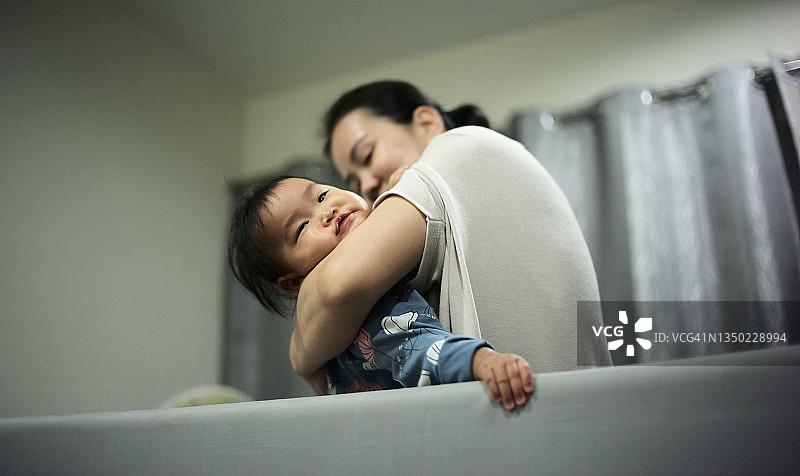 亚洲妈妈在床上玩耍，抱着6-8个月大的女儿，幸福美满图片素材
