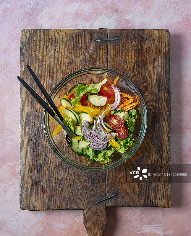 一碗新鲜的沙拉放在木砧板上，粉红色的背景图片素材