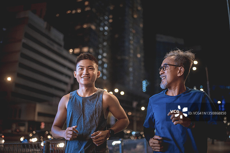 亚洲华人活跃的老人和儿子晚上下班后一起在城里跑步慢跑图片素材