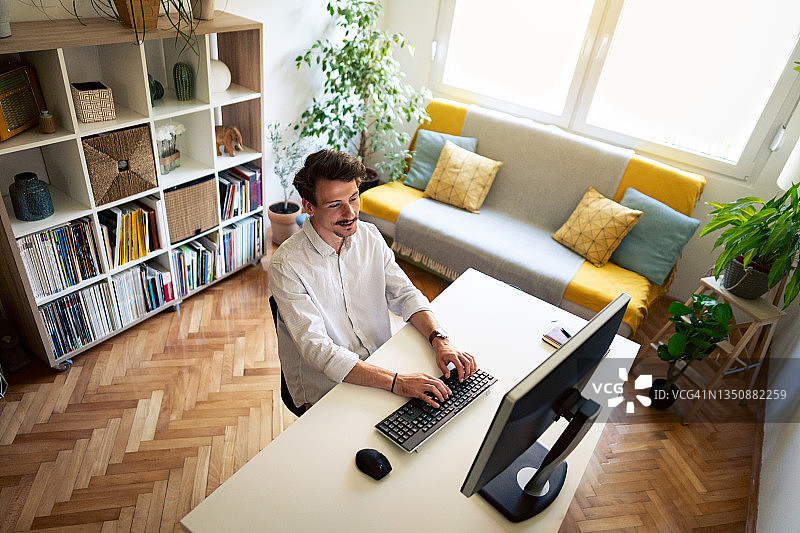 一个现代白人年轻男子的高角度视角，在他的家庭办公室的电脑上工作图片素材