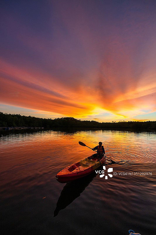 男人在美丽的夕阳下划独木舟。图片素材