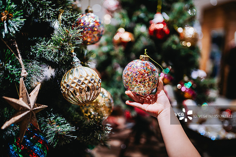 小女孩的手拿着一个五颜六色的小玩意，在圣诞节期间装饰和挂在圣诞树上。圣诞节倒计时。节日和庆典概念图片素材
