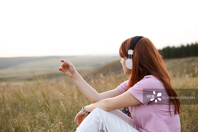 年轻的红发女子戴着耳机在聆听大自然中的音乐图片素材