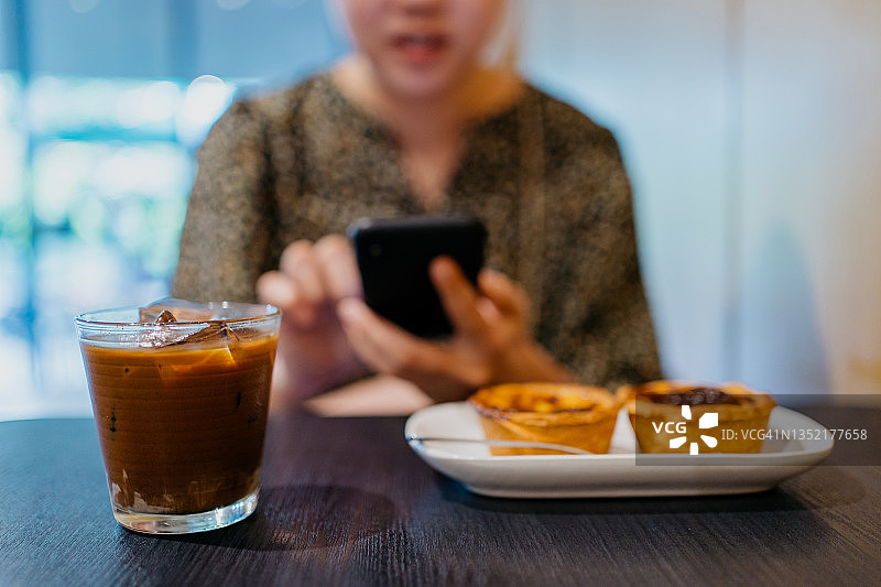 亚洲女性在咖啡馆喝咖啡，使用智能手机图片素材