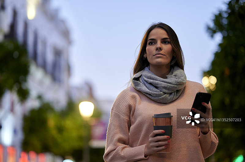 黄昏时分，一名女子在街上使用智能手机图片素材