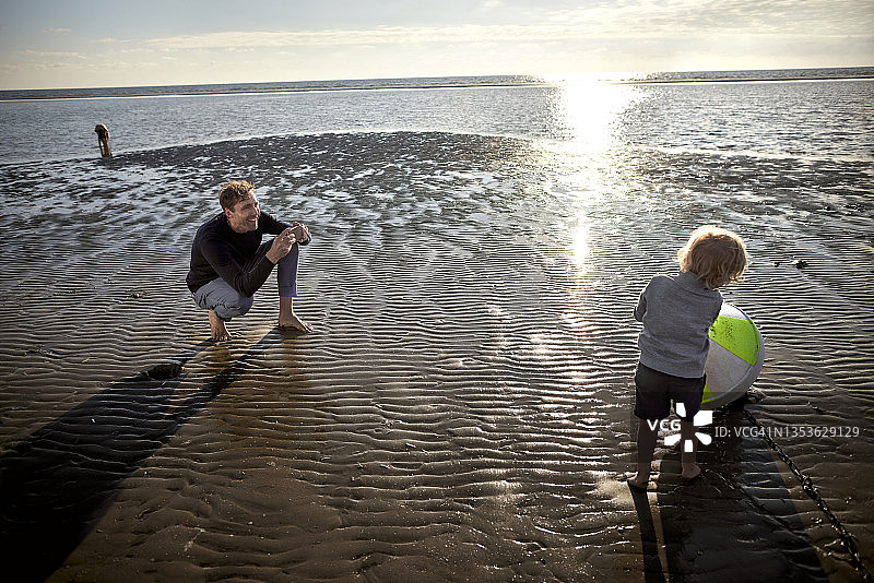 父亲用智能手机给在海滩上拿着浮标的儿子拍照图片素材