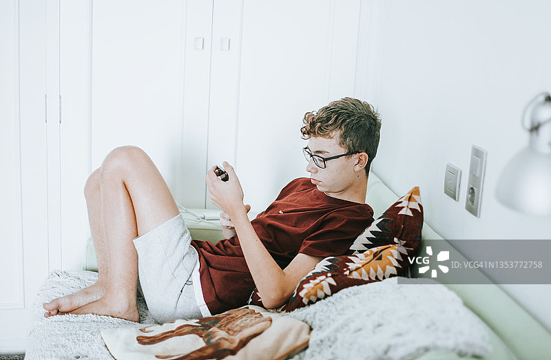 轻松的西班牙裔男性青少年在家里坐着的时候用手机发短信图片素材
