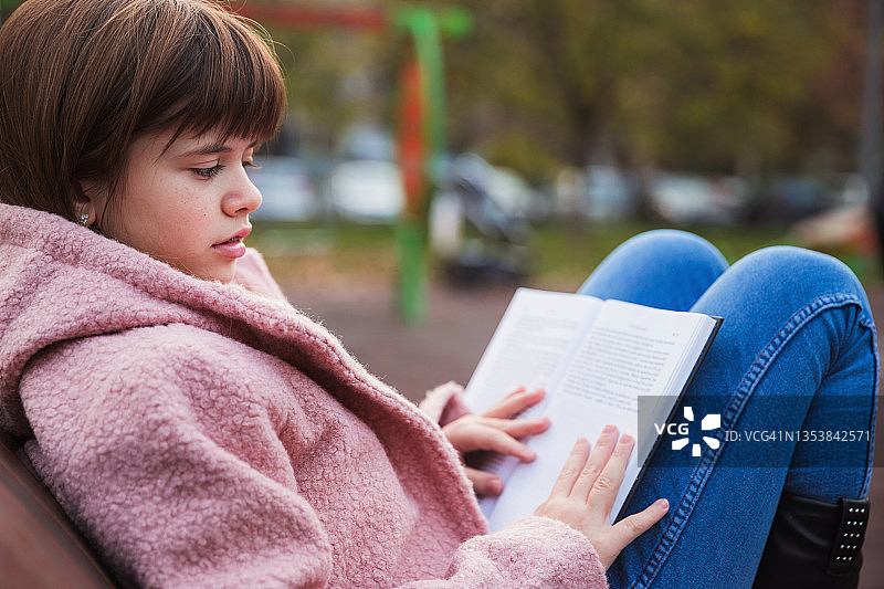 女孩坐在公园的长椅上看书图片素材