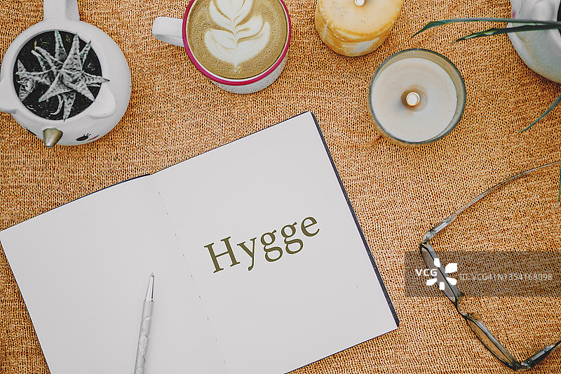 正上方是一杯咖啡，写着hygge文字的笔记本，蜡烛和多肉植物，还有棕色舒适的毯子。Hygge图片素材