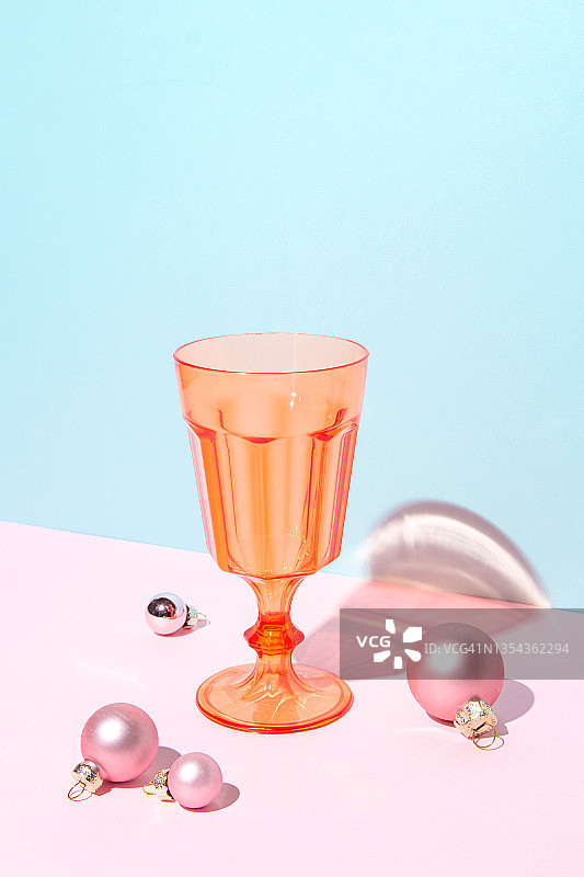 橙色葡萄酒和鸡尾酒杯在蓝色和粉红色的背景与圣诞球。色彩鲜艳的极简主义艺术构图。圣诞节和新年节日派对的概念。图片素材