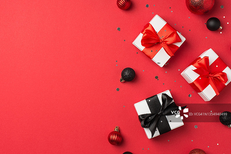 俯视图照片白色礼品盒红色和黑色丝带蝴蝶结圣诞树球和亮片在孤立的红色背景与copyspace图片素材