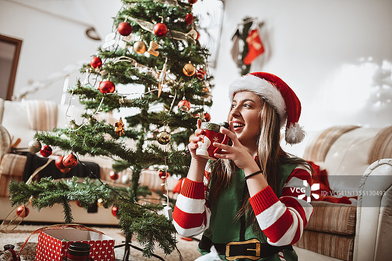 微笑的女性在客厅的树下喝茶庆祝圣诞节图片素材