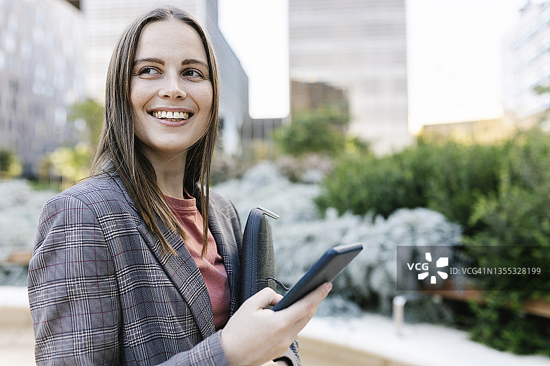 一个拿着手提电脑包和手机的快乐女人站在城市的大街上图片素材